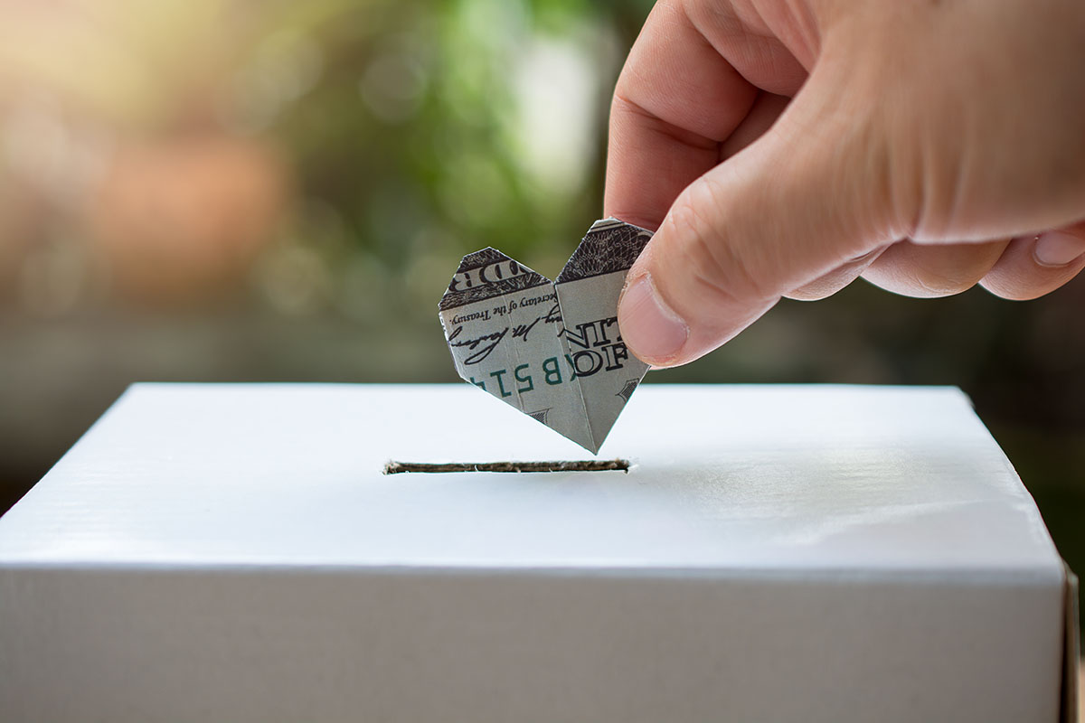 hand holding heart shape money, putting it into a donation box